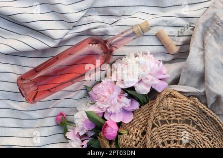 Bouteille de vin rose près du sac de paille avec de belles pivoines sur une couverture légère, plat Banque D'Images