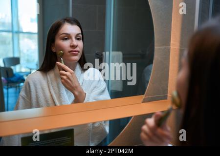 Une jolie femme se tient dans le miroir avant pour se faire masser le visage Banque D'Images