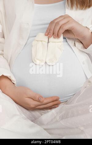 Femme enceinte avec chaussettes de bébé sur le lit, gros plan Banque D'Images