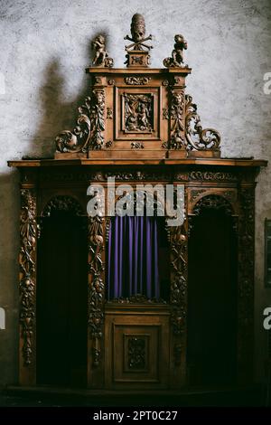 Ancienne cabine de confession typique en bois dans une église, avec des rideaux bleus. Banque D'Images