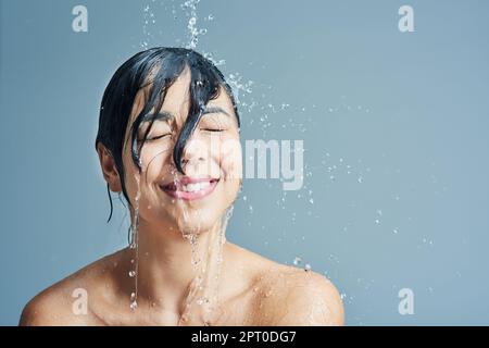 Réveillez ses sens avec une douche rafraîchissante. une jeune femme ayant une douche rafraîchissante sur fond bleu Banque D'Images