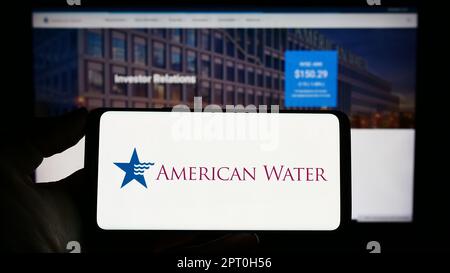 Personne tenant un téléphone cellulaire avec le logo d'American Water Works Company Inc. À l'écran devant la page Web d'affaires. Mise au point sur l'affichage du téléphone. Banque D'Images