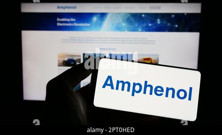 Personne tenant un smartphone avec le logo de la société américaine d'électronique Amphenol Corporation à l'écran devant le site Web. Mise au point sur l'affichage du téléphone. Banque D'Images