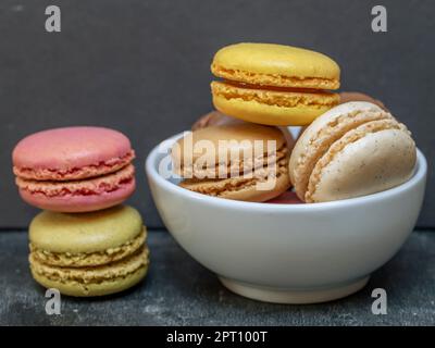 Macarons colorés dans un bol blanc à côté d'une pile de deux Banque D'Images