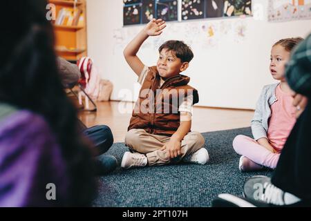 Un enfant du primaire intelligent lève la main pour donner une réponse en classe. Petit garçon participant à une leçon à l'école. Enfants de l'école primaire si Banque D'Images