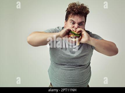 Rien ne vaut un bon hamburger. Photo studio d'un homme en surpoids qui se mord dans un hamburger Banque D'Images