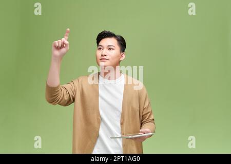 Portrait d'un homme asiatique excité tient la tablette dans sa main, lève sa main, pointe vers l'air Banque D'Images