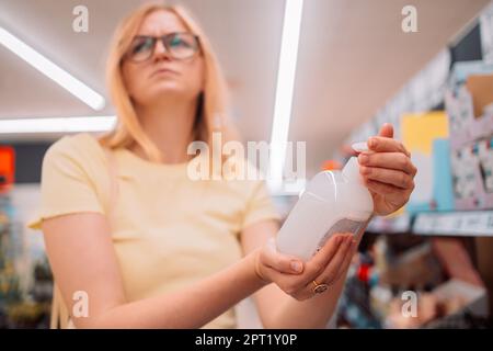 Une jeune femme souriante et gaie choisit une bouteille de savon liquide dans un supermarché Banque D'Images