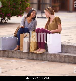 Faites vos courses jusqu'à épuisement. Deux jeunes femmes discutant sur les marches après une longue et réussie journée de shopping Banque D'Images