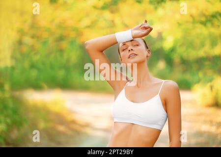 Épuisé mais je me sens super. une femme essuyant la transpiration de son front pendant qu'elle est dehors pour un jogging dans le parc Banque D'Images