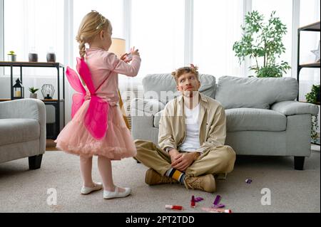 Fille faisant le cliché de son père épuisé avec maquillage drôle et la coiffure, drôle passe-temps à la maison avec des parents Banque D'Images