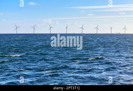 Mer avec une rangée d'éoliennes offshore à distance par jour ensoleillé. Banque D'Images