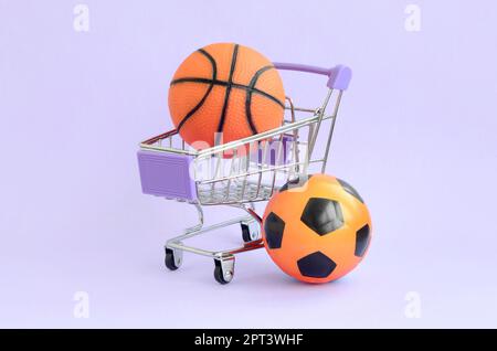 Le basket-ball et le soccer ball orange dans votre panier sur violet. Le concept de vente d'équipement de sport, de prévisions pour des matchs de sport, paris sportifs Banque D'Images