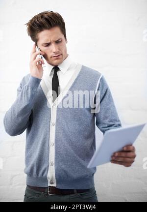 Permettez-moi de voir ce que je peux faire. Un jeune homme qui parle sur son téléphone portable tout en travaillant sur sa tablette numérique Banque D'Images