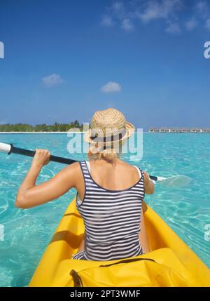 Pagayer au paradis. Une belle jeune femme pagayant sur un bateau dans un océan tropical Banque D'Images