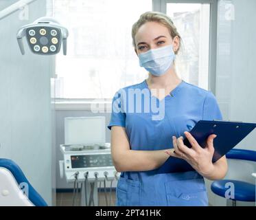 L'assistante du dentiste ou la dentiste femelle dans un masque facial protecteur sur le fond de la salle de dentisterie. Une jolie infirmière regarde la caméra avec le sourire Banque D'Images