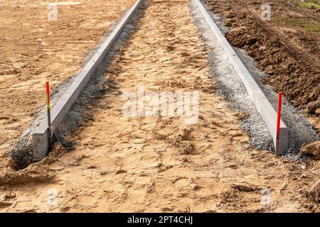 Un trottoir est en construction, un trottoir en béton est en cours d'installation et les fondations de la route sont en préparation Banque D'Images