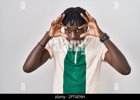 Homme africain avec des dreadlocks debout sur un fond isolé essayant d'ouvrir les yeux avec les doigts, endormi et fatigué pour la fatigue matinale Banque D'Images