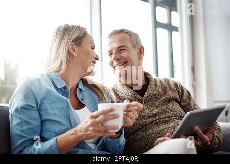 Le meilleur du confort fait maison. une femme mûre boit du café tandis que son mari utilise une tablette numérique sur le canapé à la maison Banque D'Images