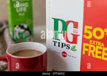 Londres. ROYAUME-UNI- 04.19.2023. Gros plan d'une grande boîte de sachets de thé PG Tips avec une tasse de thé au lait et de lait en arrière-plan. Banque D'Images