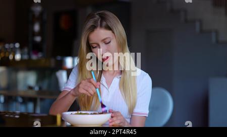 Gros plan sur une jolie jeune femme blonde mangeant dans le restaurant seul et de bonne humeur. Caucasienne joyeuse femme ayant déjeuner ou dîner dans le café. Luxe Banque D'Images