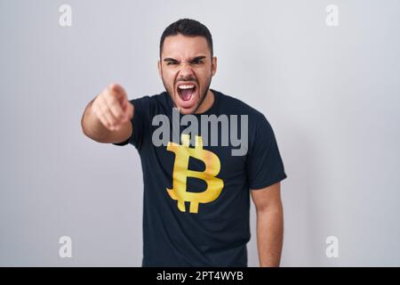 Jeune homme hispanique portant le t-shirt bitcoin pointant déplu et frustré à l'appareil photo, en colère et furieux avec vous Banque D'Images