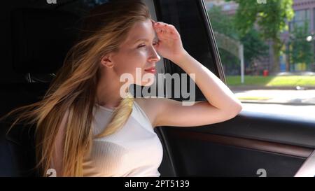 Gros plan d'une jolie femme blonde blanche et gaie assise à l'arrière dans une voiture en ville. Portrait. Bonne belle femme voyageant en auto Banque D'Images