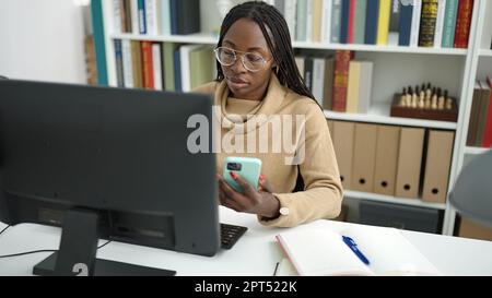 Femme africaine utilisant un ordinateur prenant des notes avec un smartphone à l'université de bibliothèque Banque D'Images