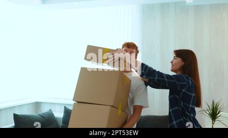 Jeune homme caucasien à cheveux rouges tenant de nombreuses boîtes en carton dans les mains et femme en mettant une autre sur le dessus. Gros plan. Couple déménagements de l'appartement Banque D'Images