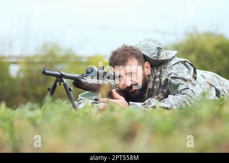 Le chasseur cherche et prend des photos avec un tireur d'élite sur un fusil de chasse, allongé sur l'herbe. Banque D'Images