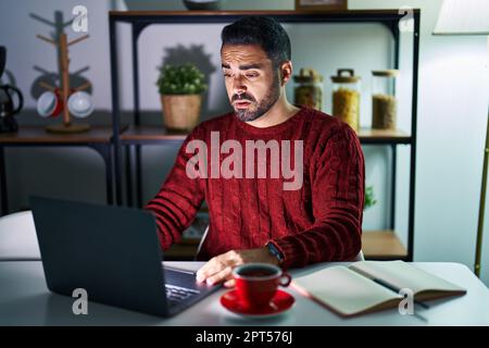 Jeune homme hispanique avec la barbe en utilisant l'ordinateur portable la nuit à la maison regardant endormi et fatigué, épuisé pour la fatigue et la gueule de bois, les yeux paresseux dans la Mo Banque D'Images