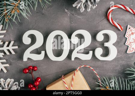 Bonne année 2023. Le bois blanc n° 2023 se trouve sur une surface en béton gris et inégal avec des branches et des décorations d'arbres de Noël, de la lipop et de la neige Banque D'Images