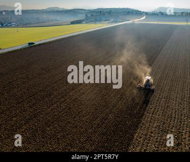 un agriculteur qui conduit un tracteur à chenilles tire un nuage de poussière derrière lui, labour, casse-croûte de surface de hersage pour faciliter la naissance et l'ensemencement o Banque D'Images