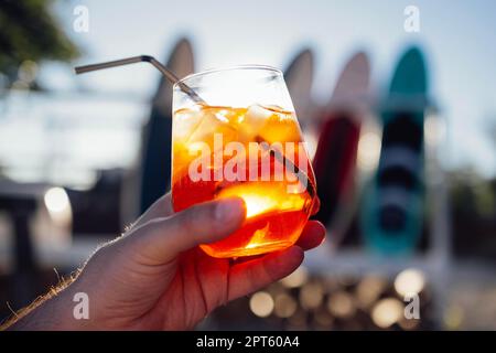 Tranche d'orange et apéritif spritz cocktail sur une pierre sur fond d'une plage de sable. Homme tenant le slass avec de l'eau minérale gazeuse aux agrumes glacés Banque D'Images