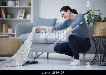 Femme, nettoyage à la maison et avec un balai balayant le tapis pour les tâches quotidiennes, la propreté et les travaux ménagers. Les femmes de ménage, les femmes de ménage et les femmes remplissent les fonctions, clun Banque D'Images