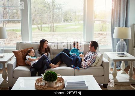 La maison est où l'amour vit. une jeune famille heureuse de quatre personnes se détendant ensemble sur le canapé à la maison. Banque D'Images