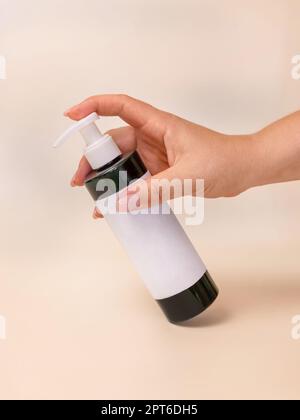 Une femme pompe à la main le liquide désinfectant d'une bouteille avec une étiquette vierge sur beige clair, gros plan, maquette. Concept de protection de la santé. Soin de la peau beauté p Banque D'Images