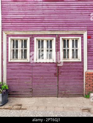 Le grunge de bois a traversé la porte abandonnée peinte en violet, avec trois fenêtres en bois blanc peintes en blanc, dans une allée pavée Banque D'Images