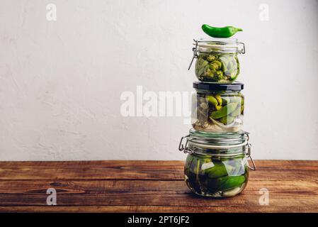 Trois jarres en verre de poivrons Jalapeno fraîchement en conserve avec herbes et ail sur une table en bois. Copier l'espace Banque D'Images