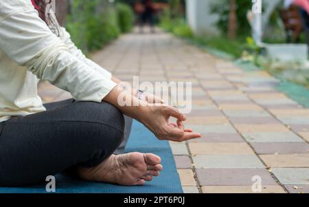 Gros plan femme mudra main geste faisant yoga détente en position lotus assis sur le tapis. À l'extérieur. Pratiquer la méditation dans la nature. Photo d'arrière-plan. Banque D'Images
