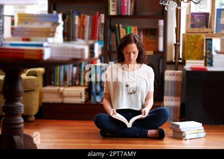 Apprécier son passe-temps préféré. Une jeune femme assise à l'étage d'une librairie et lisant Banque D'Images