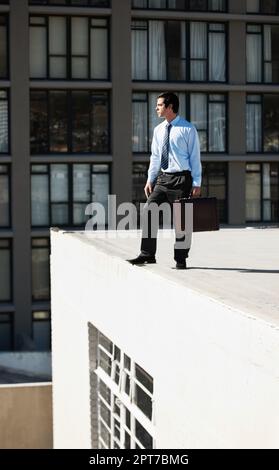 Vivre à la pointe. Un homme d'affaires se tenant sur le bord d'un toit de bâtiment Banque D'Images