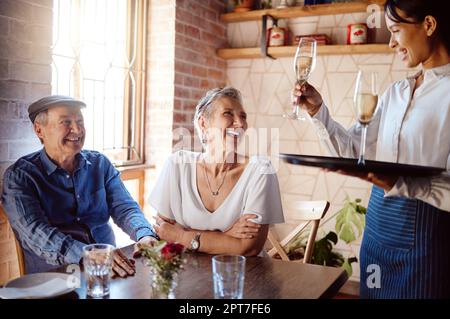 Couple senior, serveur et champagne au restaurant pour les anniversaires de mariage, les fêtes ou les anniversaires. Un homme et une femme heureux et âgés sourient avec une serveuse an Banque D'Images