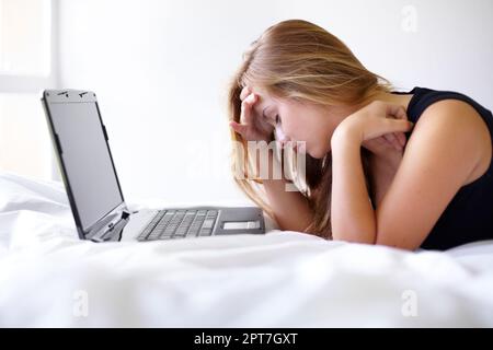 Ma tête a l'impression d'exploser. une belle jeune femme qui a l'air frustrée d'utiliser un ordinateur portable sur son lit Banque D'Images