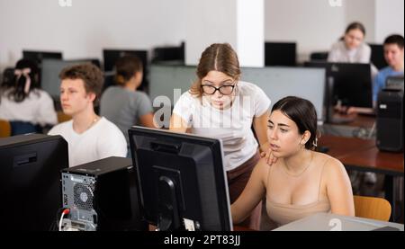 Portrait d'une jeune étudiante aidant son amie à étudier en classe informatique à l'aide d'un pc dans une bibliothèque Banque D'Images