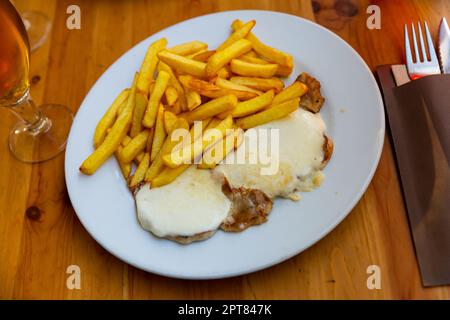 Steaks de porc nappés de mozzarella fondue servis avec des frites Banque D'Images