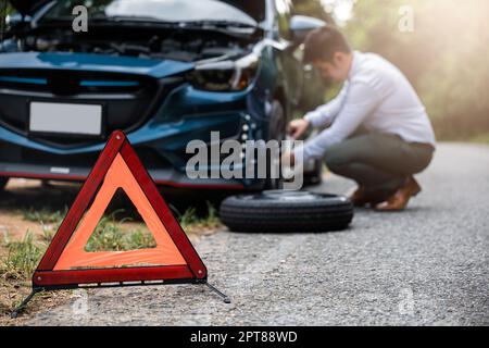 La voiture d'homme d'affaires asiatique cassée a des problèmes avec la roue de sa voiture pendant le travail le matin il change remplacer le pneu en caoutchouc sur les roues, homme d'affaires h Banque D'Images