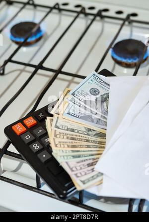 Paiement des factures de services publics, calculs sur une calculatrice. Les billets d'euro et de dollar sont près d'un brûleur à gaz en feu. Le concept d'augmenter le coût de nat Banque D'Images