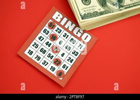 Tableau de bingo rouge ou carte à jouer pour gagner des jetons et une pile de billets en dollars. Carte de bingo classique américaine ou canadienne de cinq à cinq sur fond rouge vif Banque D'Images