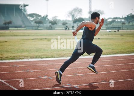 Mise en marche du relais. Tir en longueur d'un jeune athlète masculin de belle taille qui court avec un bâton pendant une course de relais Banque D'Images